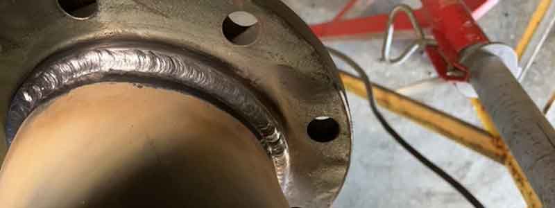 Close-up of a metal pipe joint with visible weld seam; parts of surrounding equipment and floor are also visible in the background.