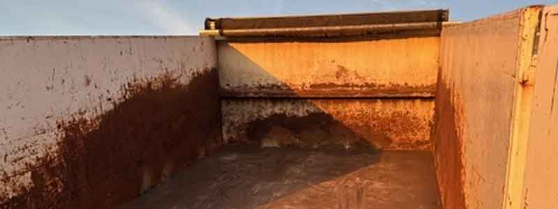 The image shows the interior of an empty, rusty metal container or dumpster with sunlight casting shadows on its walls.