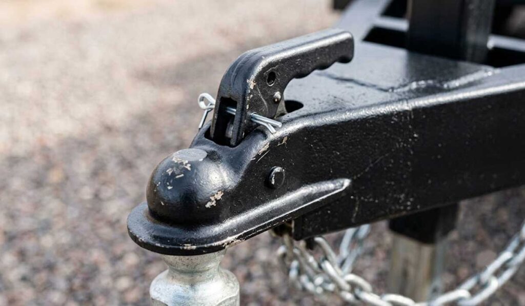 Close-up view of a trailer hitch coupler secured onto a tow ball, with a safety pin and chains visible.